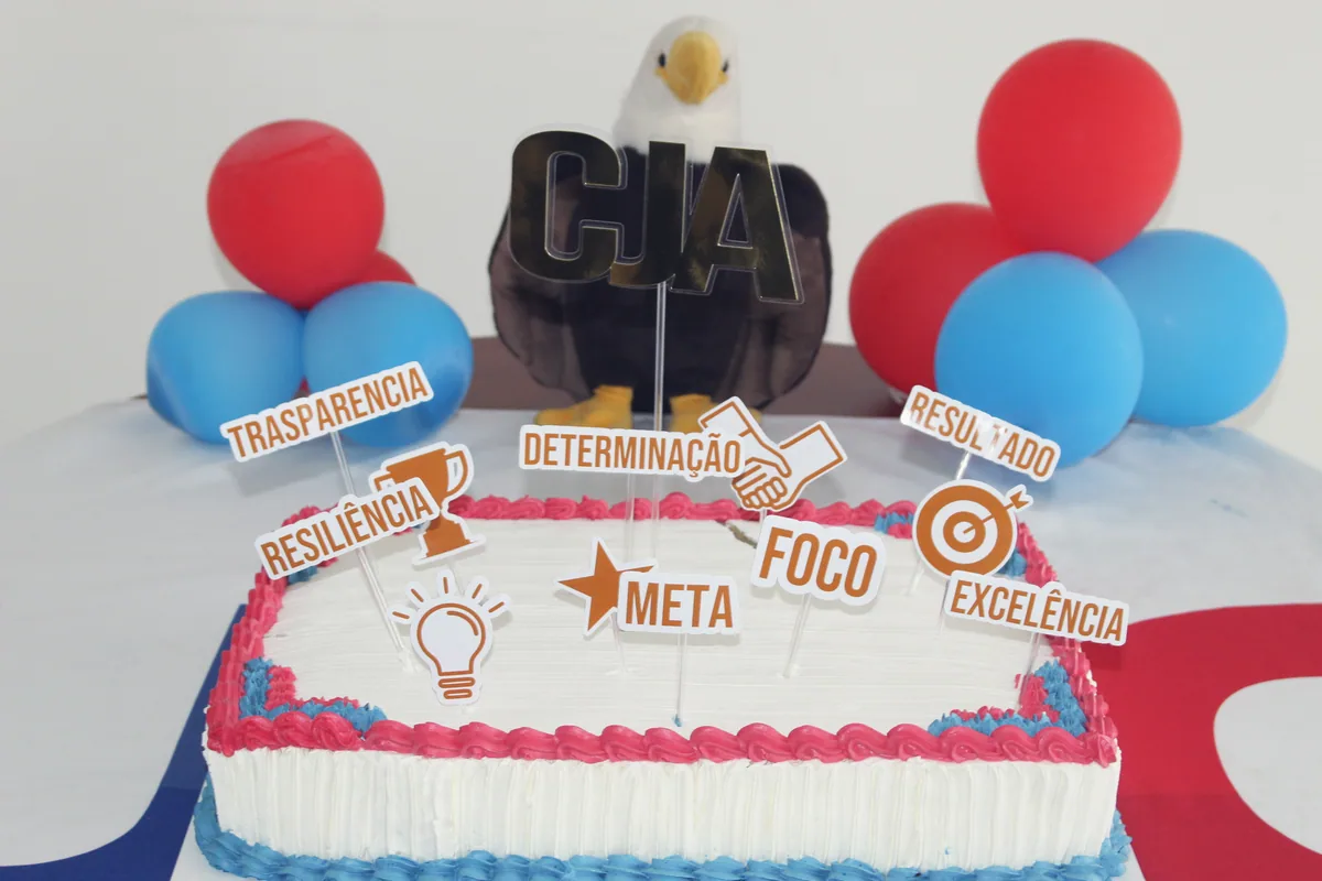 O bolo dos 33 anos da CJA com plaquinhas dos valores: Transparência, Determinação, Resiliência, Foco, Meta, Excelência e Resultado.
