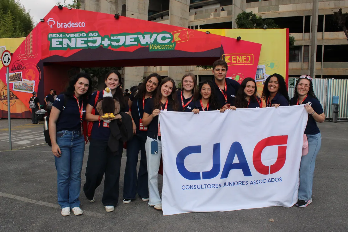 Onze membros da CJA de polo azul-marinho seguram a bandeira da CJA na entrada do ENEJ 2026, em Belo Horizonte.